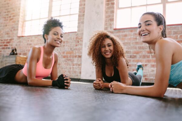 three young women in fitness class looking at camera and smiling